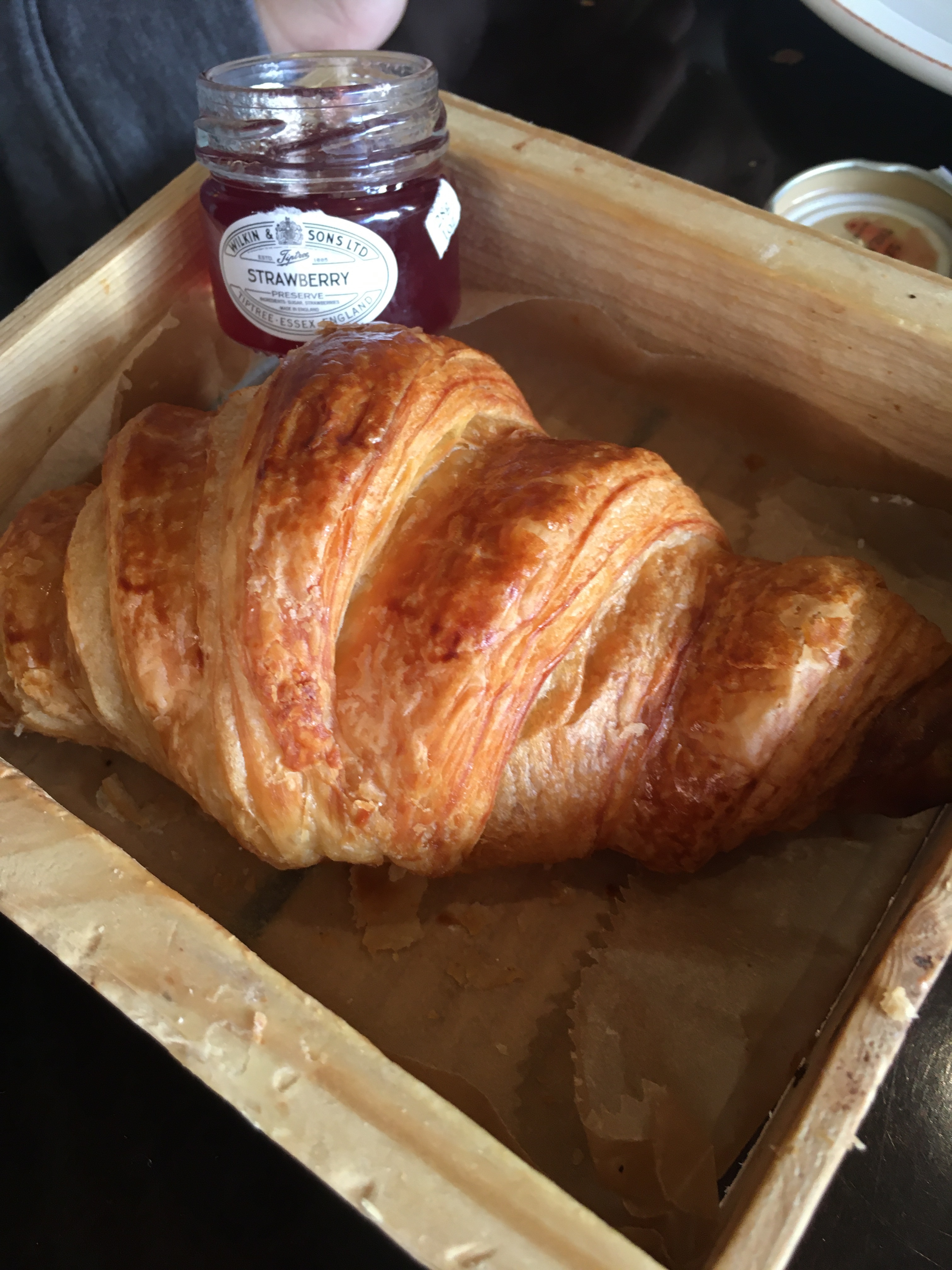 croissant in wooden tray with tiny jar of strawberry preserves