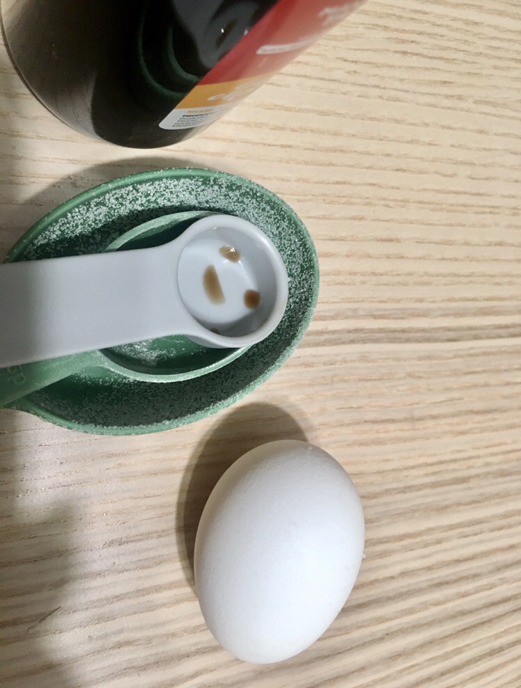 an egg and measuring cups, one with a happy face formed by vanilla extract