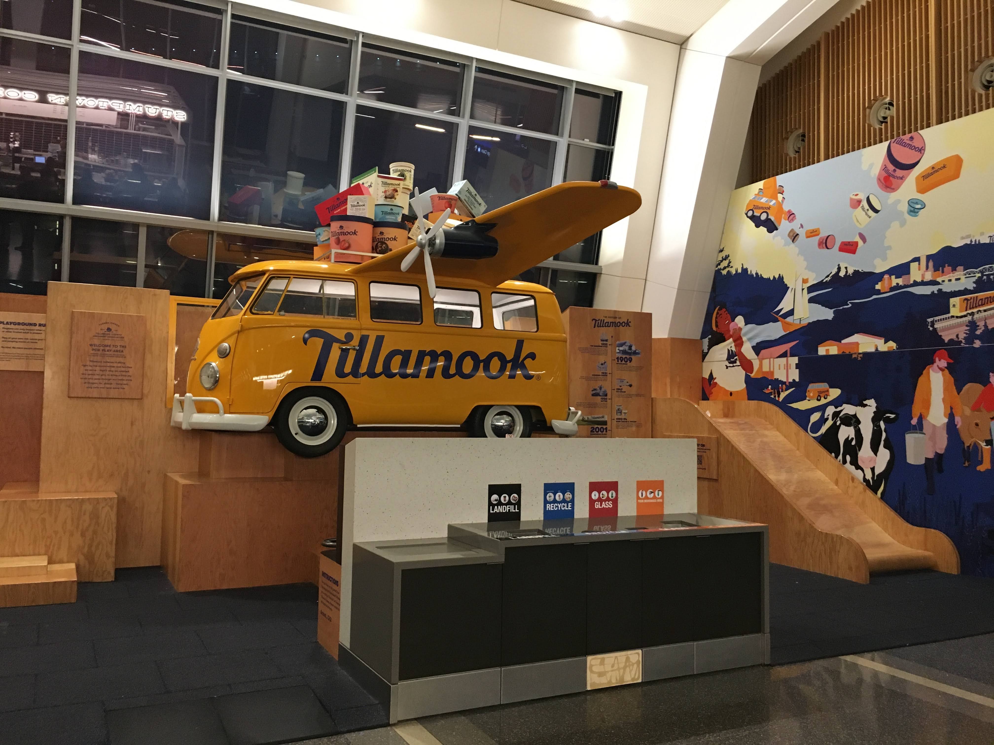 indoor play area with yellow van with the name Tillamook in blue letters next to wooden slide and steps 