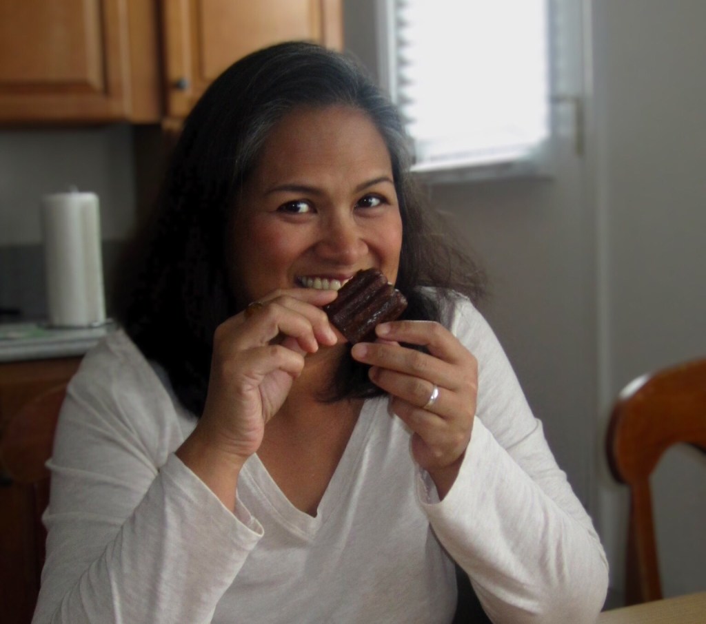 smiling woman holding canelé brown pastry near mouth photo by Jennifer Alvarez