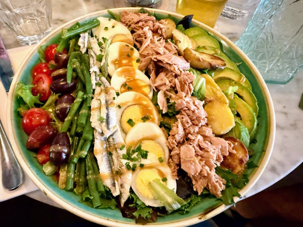 cherry tomatoes, black olives, green beans, sardines, sliced hard boiled eggs, tuna, potatoes, avocado slices on a bed of green lettuce