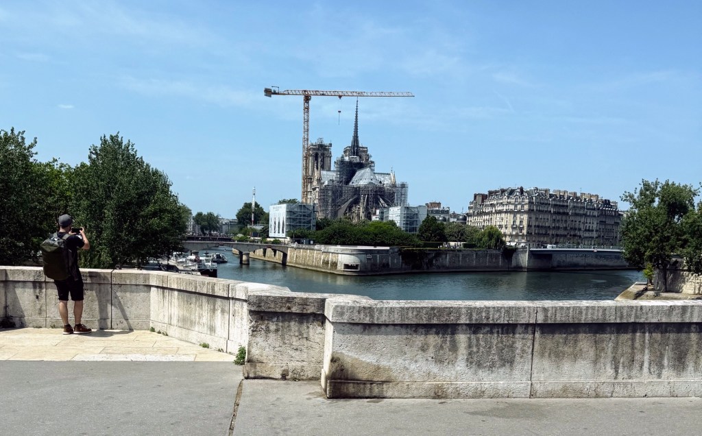 man taking photograph of cranes and scaffolding around Notre Dame Cathedral in Paris photo by Darlene taken June 2025